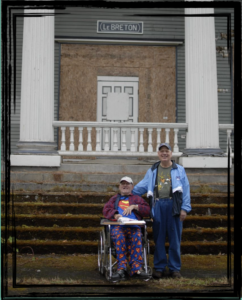Two men, one in a wheelchair, in front of a boarded up building