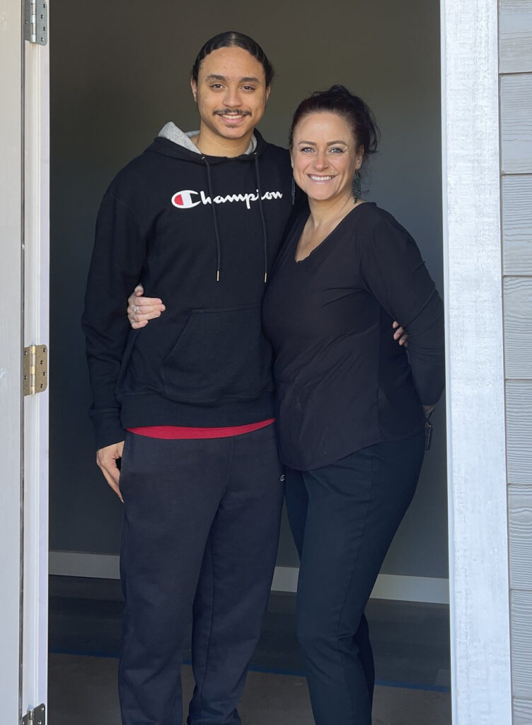 A smiling tall young man and his smiling mother stand in a doorway