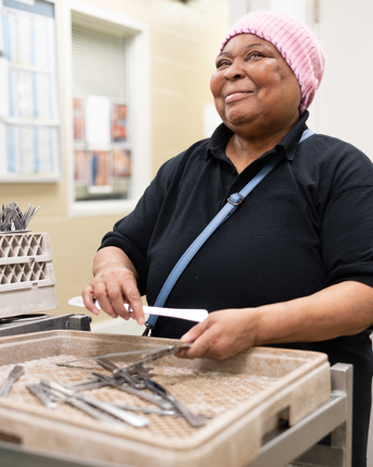 A smiling Black woman wearing a pink beanie holds recently washed silverware