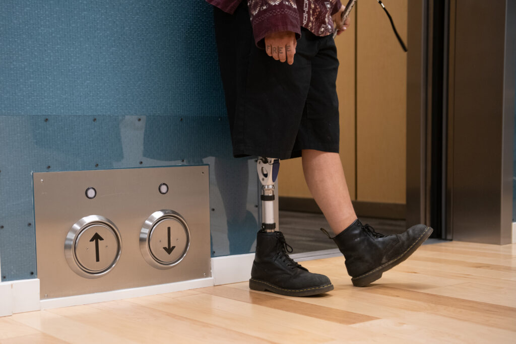 A person with a prosthetic leg stands next to an elevator with a kickplate