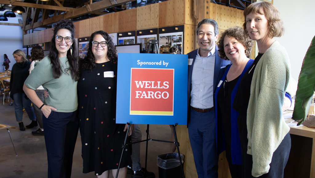 A happy group of people standing around a sign that says "Wells Fargo"