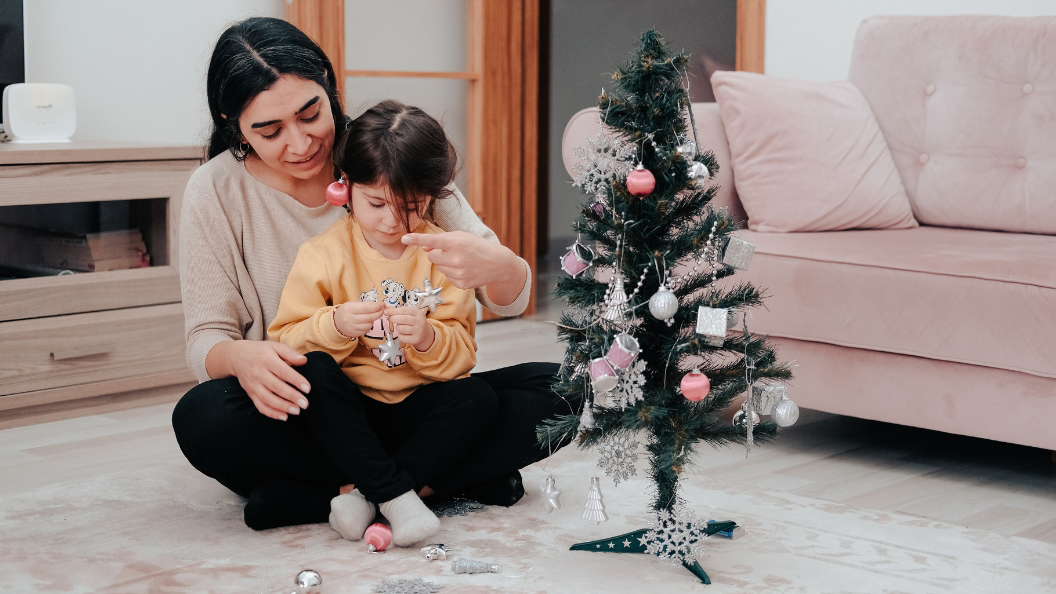 A mother and child decorate a small Christmas tree