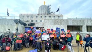 Dozens of people gather in front of a Capitol building holding signs