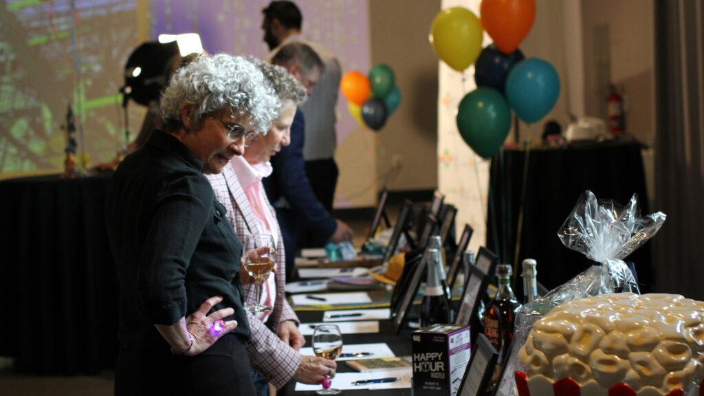 Two people look at silent auction items displayed on a long table