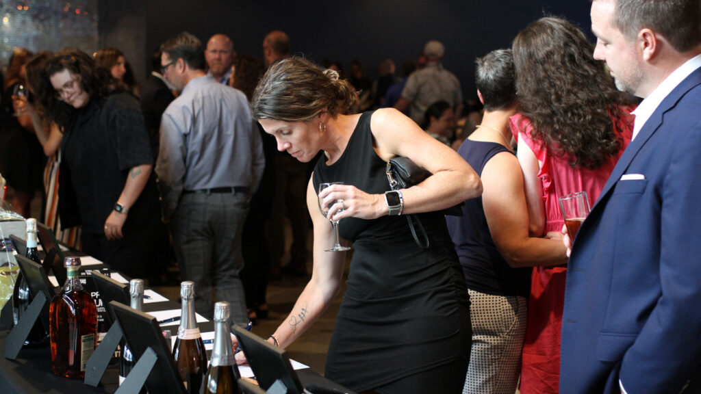 A woman in a black cocktail dress makes a bid on a silent auction item