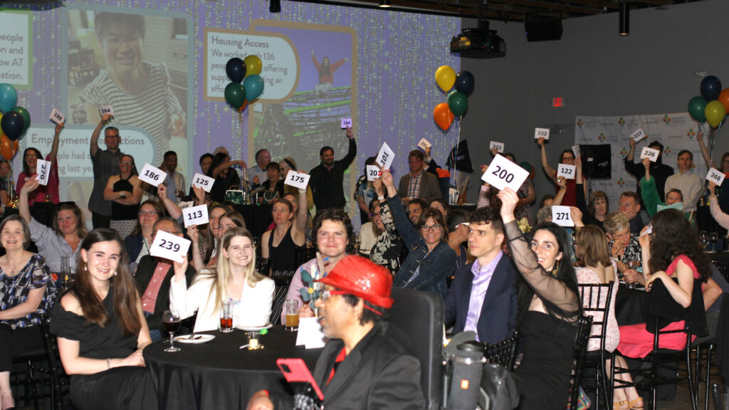 People dressed up in party clothes hold up bid numbers and smile