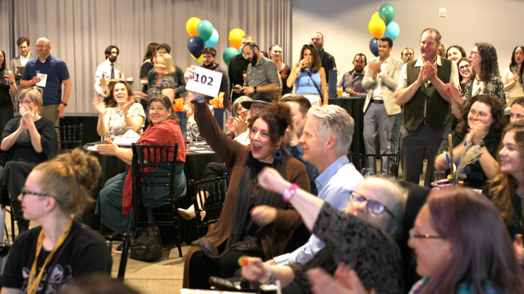 People in party clothes applaud as one woman holds up a bid number