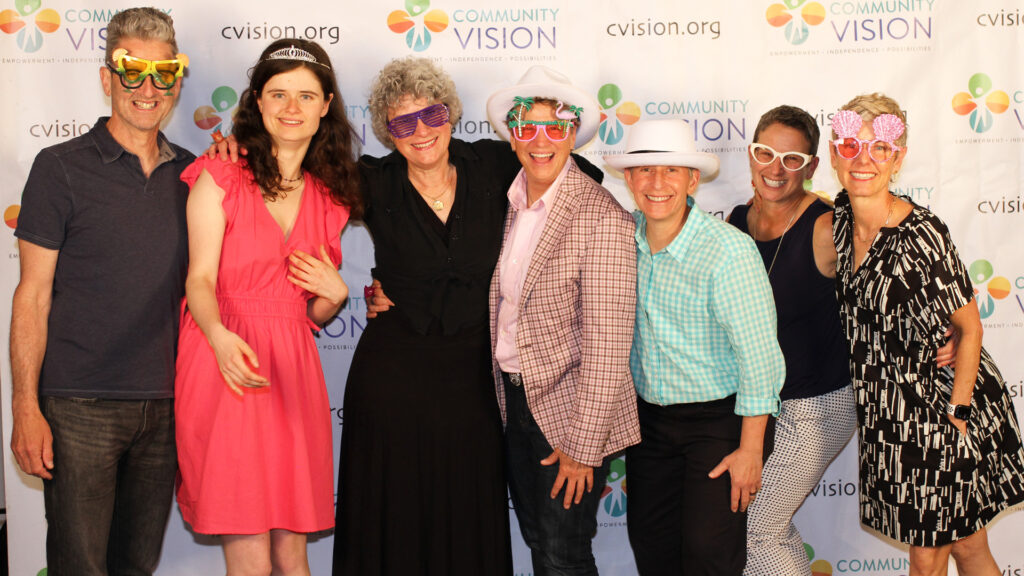 Group photo of smiling family members and friends in front of a Community Vision backdrop
