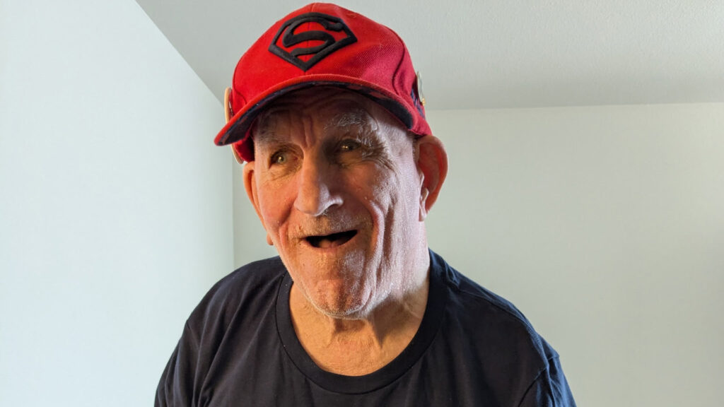 Older man in red Superman baseball cap smiles for a photo