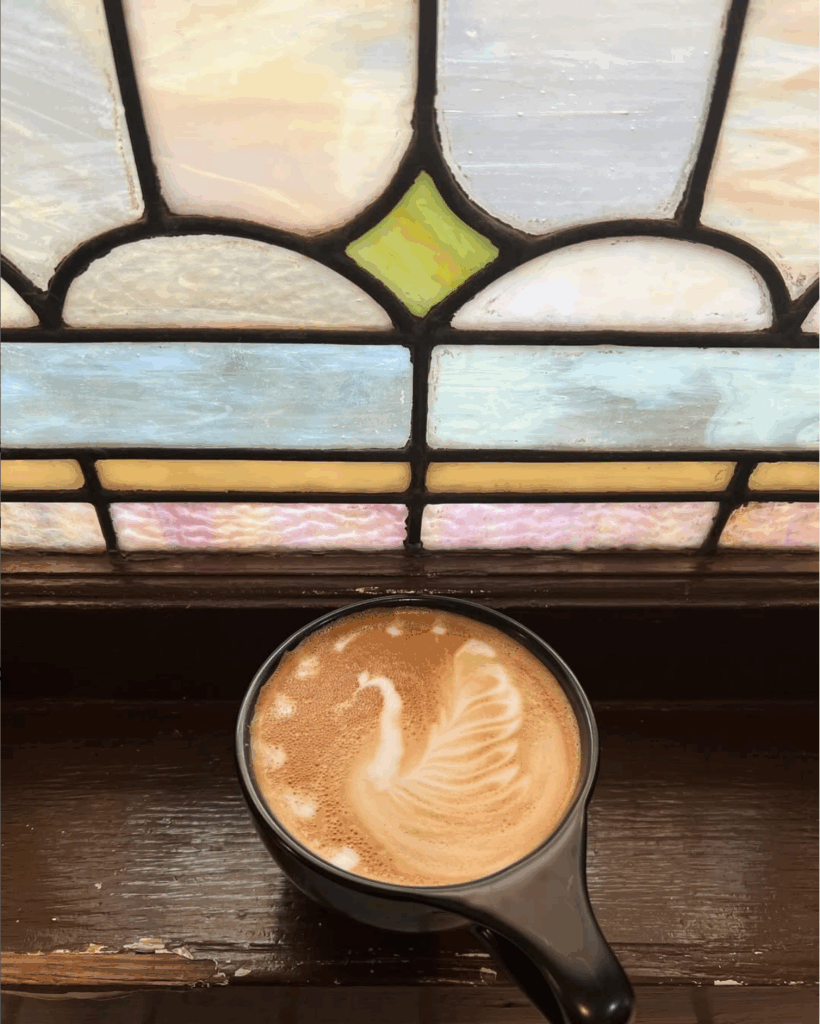 Cappuccino on a worn, dark-wood ledge of a stained-glass window