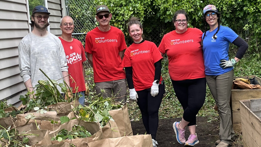a group of six people stand in a backyard with bags full of cleared green plants