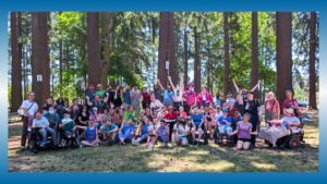 A group of people of varying abilities and backgrounds pose for a group shot at a summer picnic