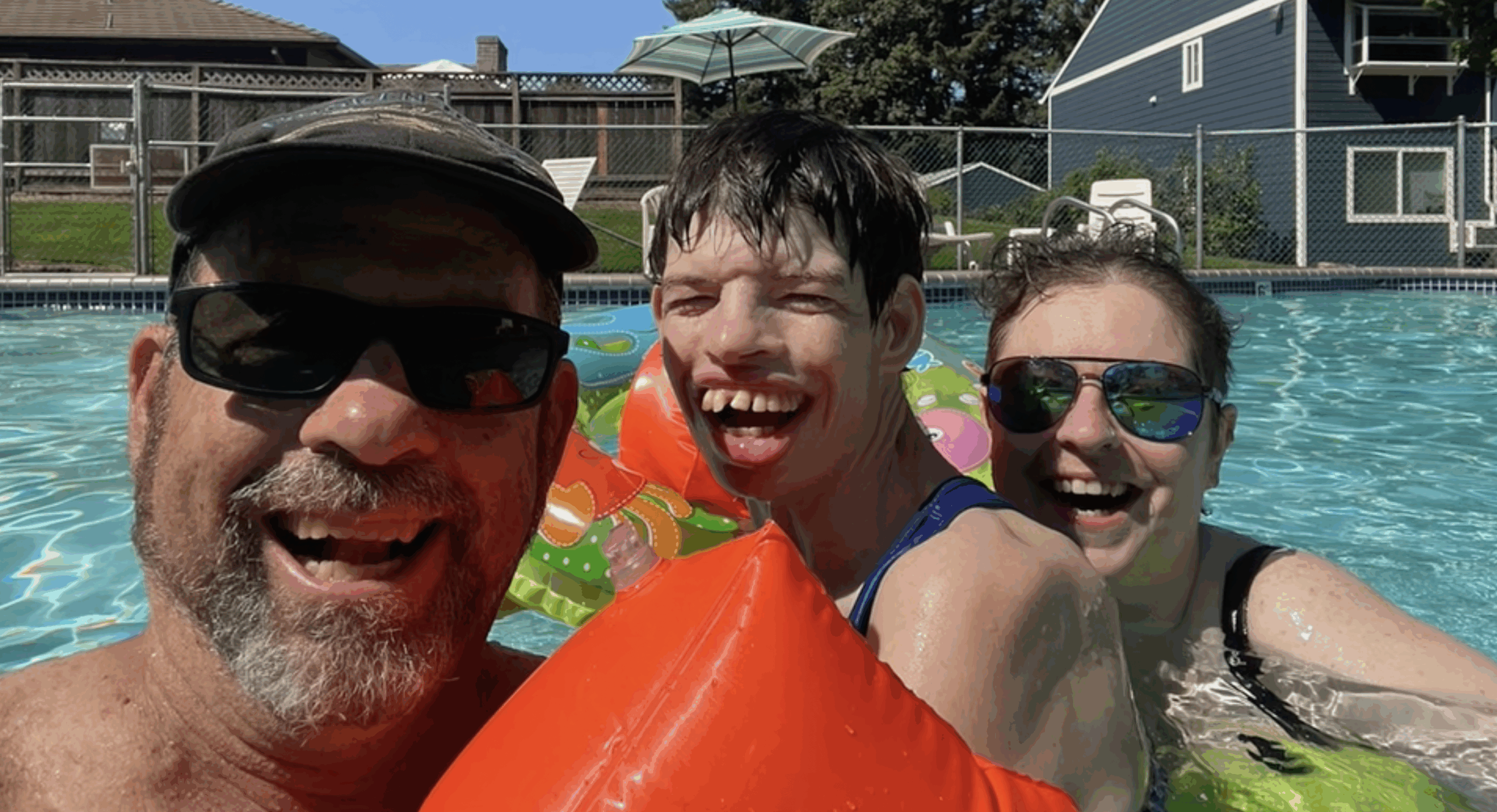 Three people smiling and playing in a swimming pool with inflatables
