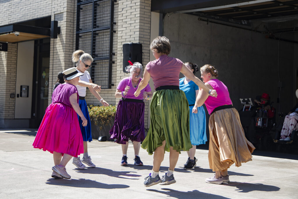 _Z3A9516.jpg Six women wearing colorful flowy long skirts dancing in a circle.
