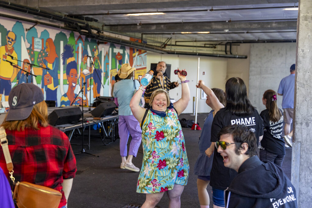 People dancing next to a stage that is in front of a colorful mural.