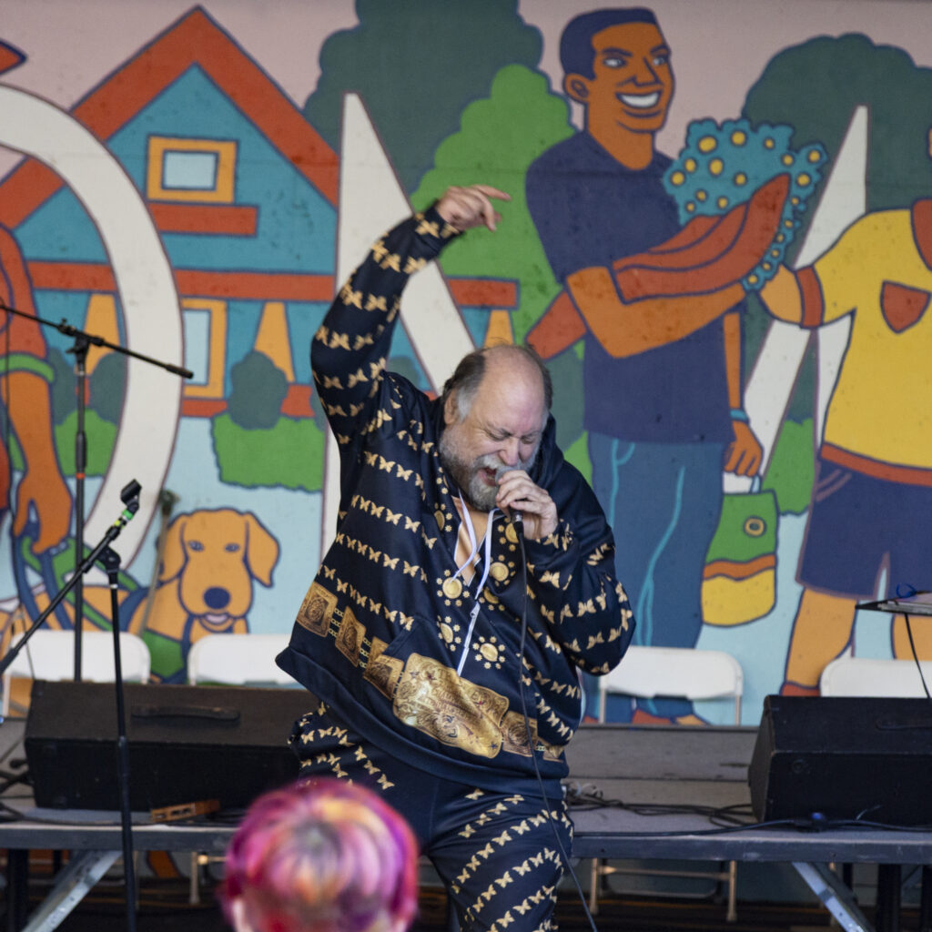 _Z3A9864 Man in a navy and gold sweat suite sings into a microphone.